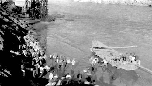 People loading packs into boat on river, near waterwheel