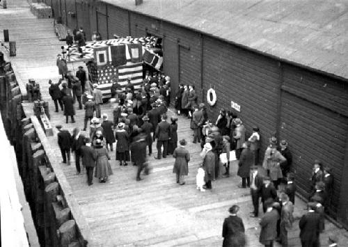 People on pier, buildings, stand with flags