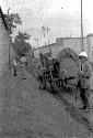 One man pushing cart on rutted road, three others standing