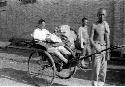 Two rickshaw pullers, third man seated in rickshaw