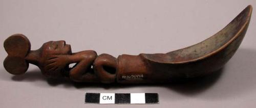 Wooden spoon, handle carved in human effigy: sitting position, elbows resting on