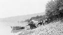 People and animals pulling cart along riverbed