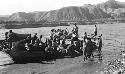 People in and next to boat in river by mountains