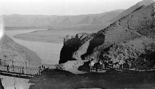 People and horses near bridge spanning river in mountains