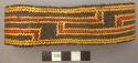 Basketry arm band; dark brown with yellow and red design