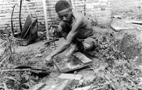 Man squatting on ground working with tools