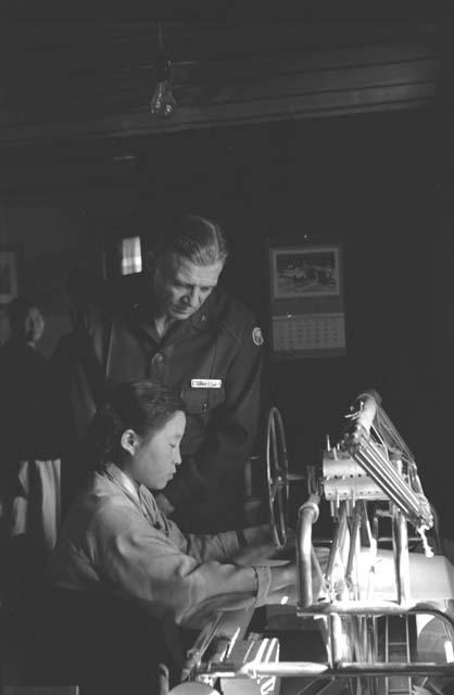 Military Man "Whitcomb" looking as young woman operates machine.