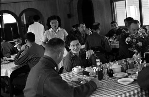 Captain Martha A. Voyles (General Whitcomb’s aide-de-camp) talking with a colleague in the mess hall as a Korean server looks on