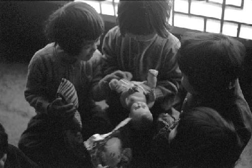 Children holding baby doll in front of window (inside)