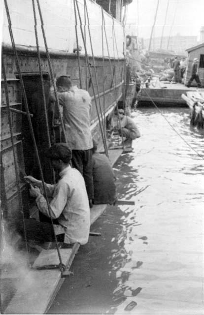 Men working on boat; titled "Salvaging boat after war"