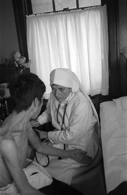 Nun with stethoscope talking with shirtless man.