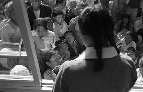 Woman with braids looking out window at crowd.