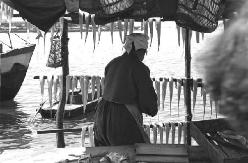 Fishmonger with back turned, port in background