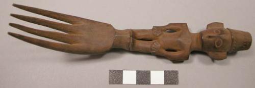 Wooden fork, 4 prongs, handle carved in human effigy: hands resting on flexed kn