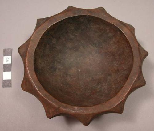 Carved, dark-colored wooden bowl with scalloped edges, base rim pierced for hang