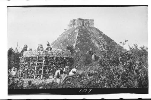 Lime Burning. Cylinder of firewood prepared, workers piling cracked limestone on