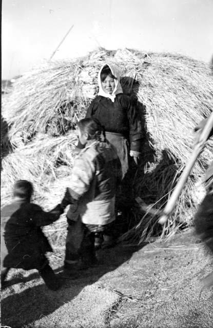 Woman and children in front of hay stack