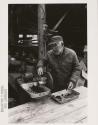 Hydaburg: Native American man grinding seaweed with a food mill