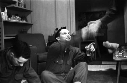 Two military men sitting on the floor; one shakes hands with third person.