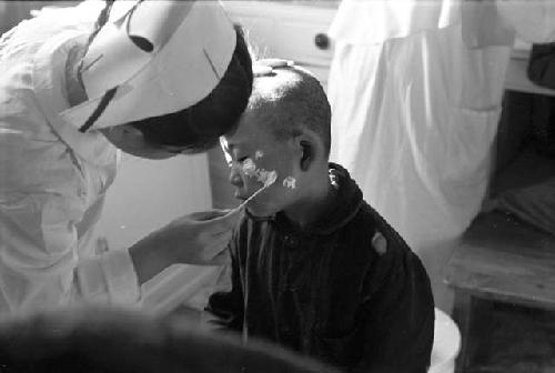 Nurse spreading ointment on child's face with cotton swab.