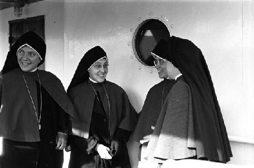 Four nuns standing in front of porthole on ship.