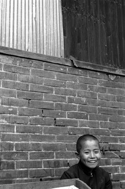 Boy dressed in black; brick wall behind him.