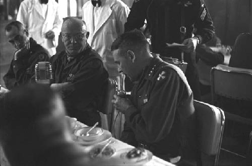 Military Men at dinner table with microphone.