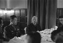 Same man at table; military officer next to him.