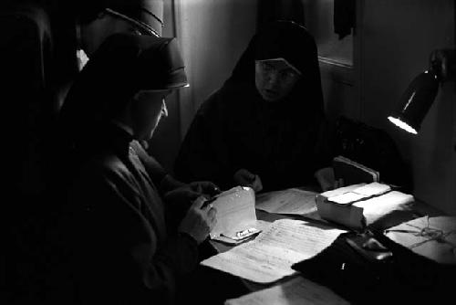 Man reading documents at desk, lit by desk lamp.