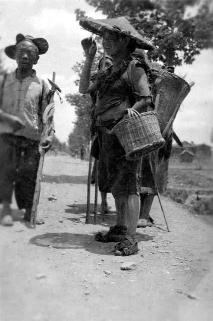 Man, woman with baskets; "Two couples (wanderers from hills) stop on roadside to