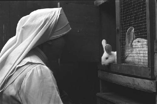 Nun holding door open to rabbit cage.