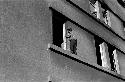 Boy with hat standing on building window ledge.