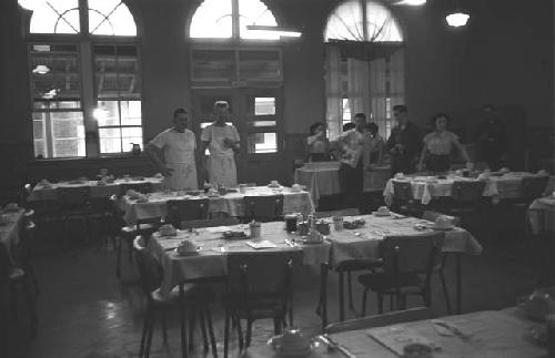 Eight people standing at back of set dining room.