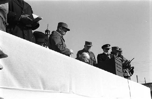 Five Military men gather around the man with glasses sitting next to podium.