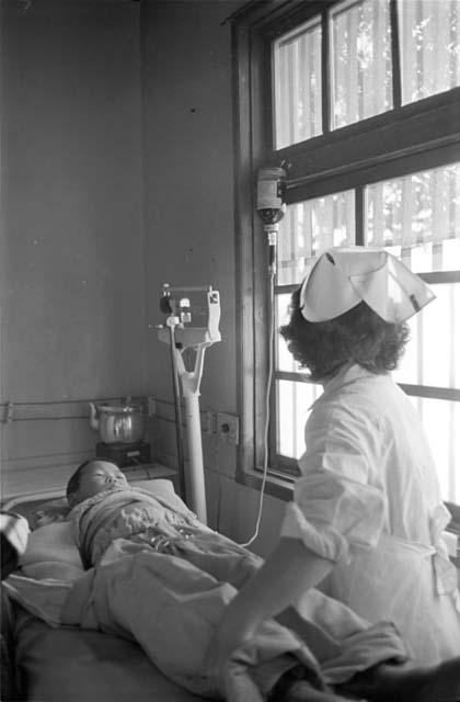 Nurse checking on child in front of window.