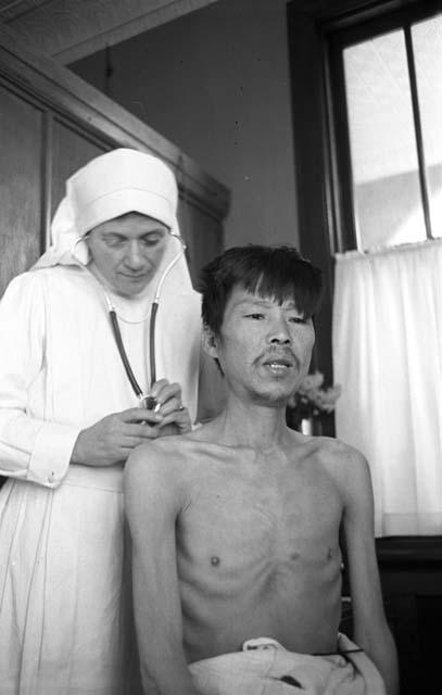 Nun using stethoscope on shirtless man.
