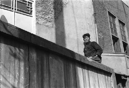 Man leaning against building, on ledge/balcony.