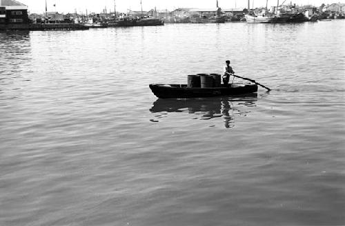 Man on boat with some buckets rowing in a harbor.