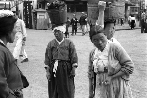 Four women with buckets on their heads on the street.