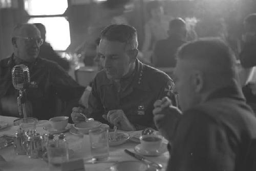 Military men sitting at table with a microphone on it, in Dining Hall.