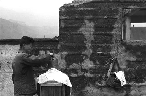 Man shaving head of customer outdoors.