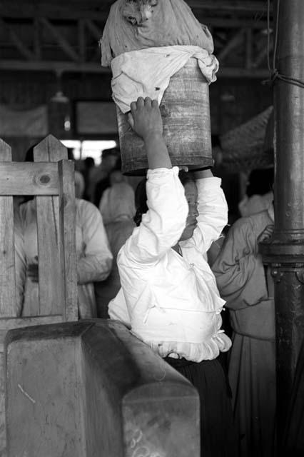 Woman holding basket on her head; more people behind her.