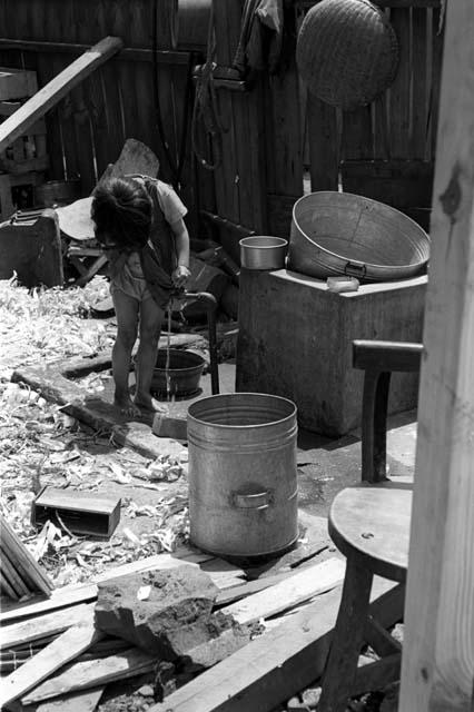 Woman using water spout in junkyard, large metal buckets.