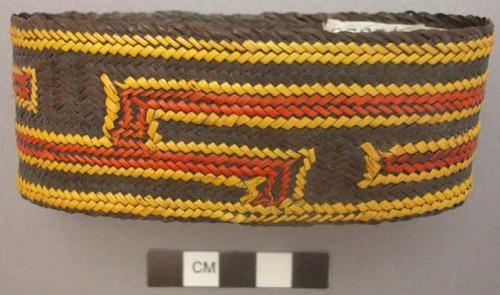 Basketry arm band; dark brown with yellow and red design