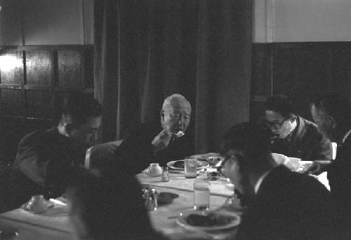 Same man at table with other men; they are eating.