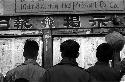 Men reading newspapers on wall of newspaper company's building