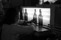 Woman leaning against counter, three empty beer bottles on counter.