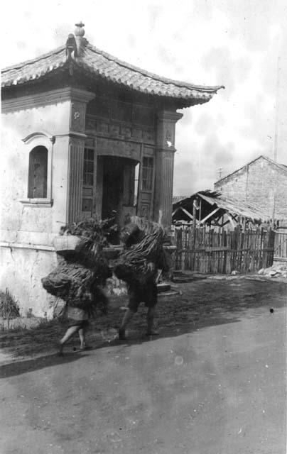 People with packs walking on a street past a building