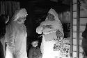 Two nuns speaking; child standing in between; one nun holds box of cloth.