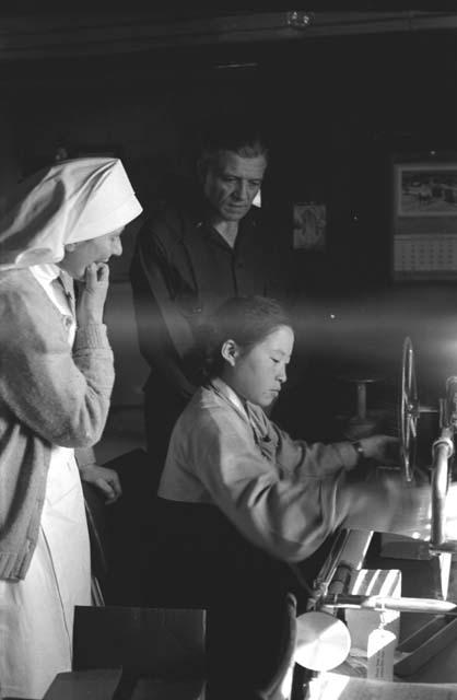 Nun and man look at young woman operate machine.